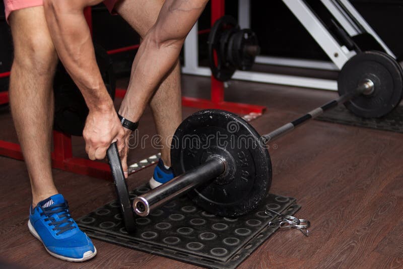 Le jeune homme dans le gymnase rassemble le barbell images stock Le jeune homme dans le gymnase rassemble le barbell images stock