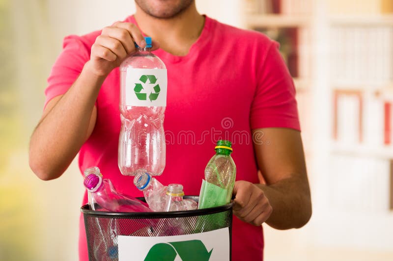 Le jeune homme de sourire mettant une bouteille en plastique à l'intérieur d'un petit éboueur noir complètement de plastique, réu images stock Le jeune homme de sourire mettant une bouteille en plastique à l'intérieur d'un petit éboueur noir complètement de plastique, réu images stock