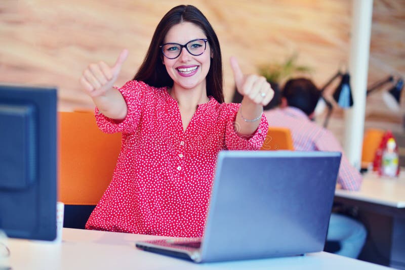 Le jeune joli ingénieur de femme s'asseyant dans le bureau au bureau avec l'ordinateur portable et montrant le pouce en tant que image libre de droits Le jeune joli ingénieur de femme s'asseyant dans le bureau au bureau avec l'ordinateur portable et montrant le pouce en tant que image libre de droits