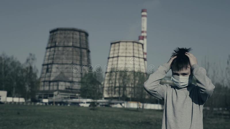 Le jeune masque de port de pollution saisit sa tête et regrets Type restant contre des cheminées d'usine clips vidéos