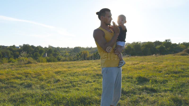 Le jeune père tient sur des mains son fils dans le pré à la nature au jour d'été ensoleillé Étreindre de papa et de petit garçon photographie stock libre de droits Le jeune père tient sur des mains son fils dans le pré à la nature au jour d'été ensoleillé Étreindre de papa et de petit garçon photographie stock libre de droits