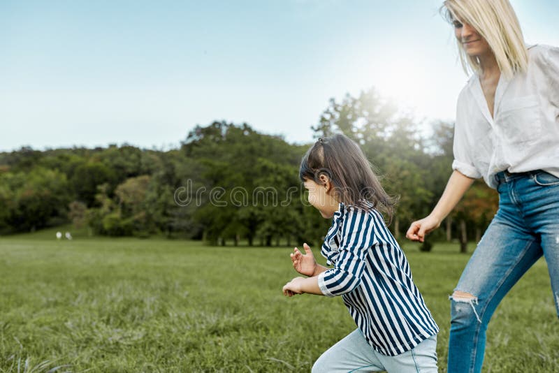 Le joli jeu heureux de petite fille m'attrapent avec sa mère sur l'herbe verte en parc Belle femme aimante et sa fille photo stock Le joli jeu heureux de petite fille m'attrapent avec sa mère sur l'herbe verte en parc Belle femme aimante et sa fille photo stock