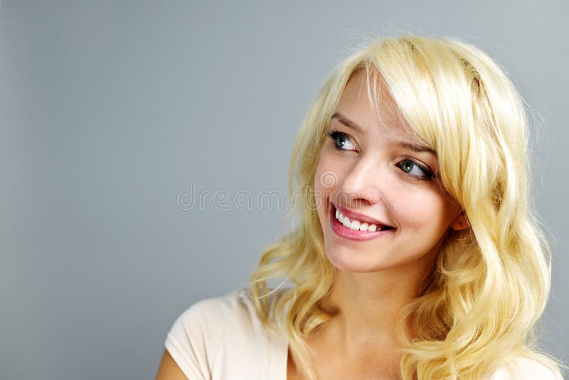 Portrait of smiling young blonde woman looking to the side on grey background. Portrait of smiling young blonde woman looking to the side on grey background