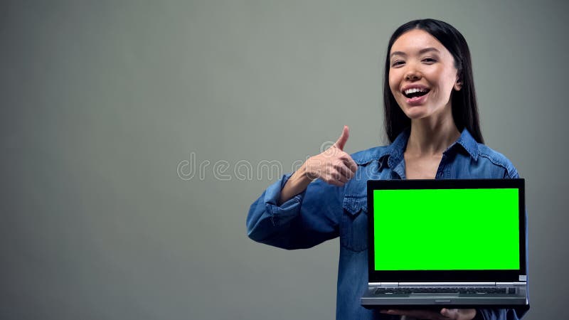 Le kvinnan som visar tummarsom rymmer den gr?na sk?rmb?rbara datorn, online-utbildning royaltyfri fotografi Le kvinnan som visar tummarsom rymmer den gr?na sk?rmb?rbara datorn, online-utbildning royaltyfri fotografi