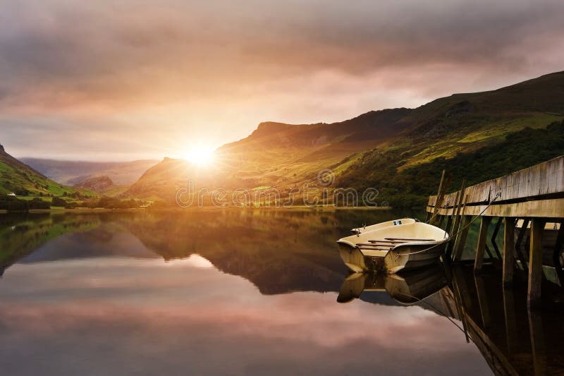 Sunrise over lake with boats moored at jetty with sun burst over mountains. Sunrise over lake with boats moored at jetty with sun burst over mountains