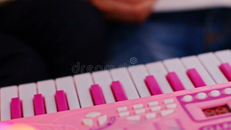 Le macro doigt de petite fille appuie sur des touches sur le piano rose de jouet