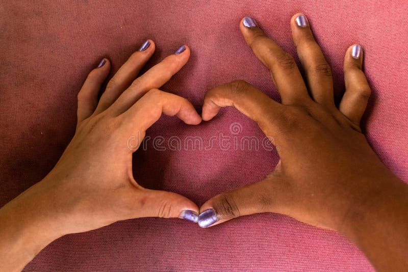 Le mani bianche e nere delle amiche formano un cuore delle dita contro il razzismo fotografia stock Le mani bianche e nere delle amiche formano un cuore delle dita contro il razzismo fotografia stock