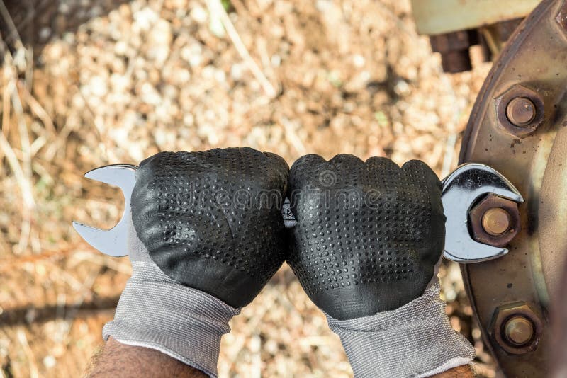 Le mani con i guanti del lavoro che tengono una chiave e stringono molto Rusty Bolts immagini stock libere da diritti Le mani con i guanti del lavoro che tengono una chiave e stringono molto Rusty Bolts immagini stock libere da diritti