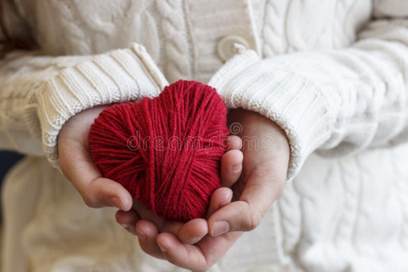 Le mani del ` s dei bambini tengono un cuore del filo rosso per tricottare fotografia stock libera da diritti Le mani del ` s dei bambini tengono un cuore del filo rosso per tricottare fotografia stock libera da diritti