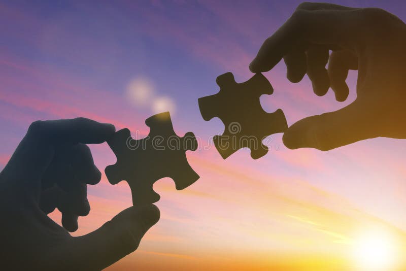Le mani di silhouettes assemblano il puzzle contro il cielo al tramonto. concetto di business. collaborazione di partnership
