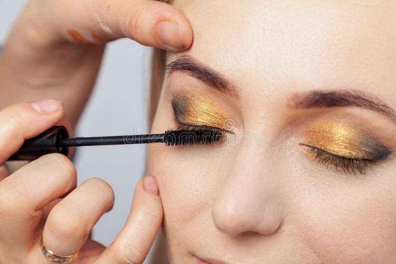 Le maquilleur met sur un maquillage de style oriental avec de l'or et les nuances vertes d'une jeune fille blonde attirante, pein image stock Le maquilleur met sur un maquillage de style oriental avec de l'or et les nuances vertes d'une jeune fille blonde attirante, pein image stock