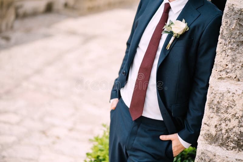 The groom in the suit with a red tie and a boutonniere with white rose on the street of the old town, close-up. High quality photo. The groom in the suit with a red tie and a boutonniere with white rose on the street of the old town, close-up. High quality photo