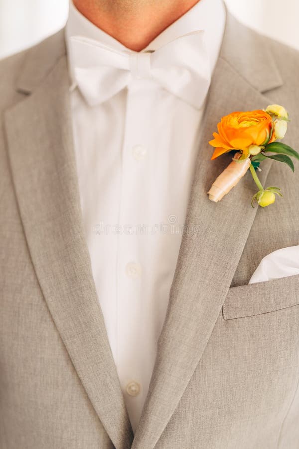 The groom in a gray suit with a white bow tie and a boutonniere with orange flowers in a hotel room, close-up. High quality photo. The groom in a gray suit with a white bow tie and a boutonniere with orange flowers in a hotel room, close-up. High quality photo