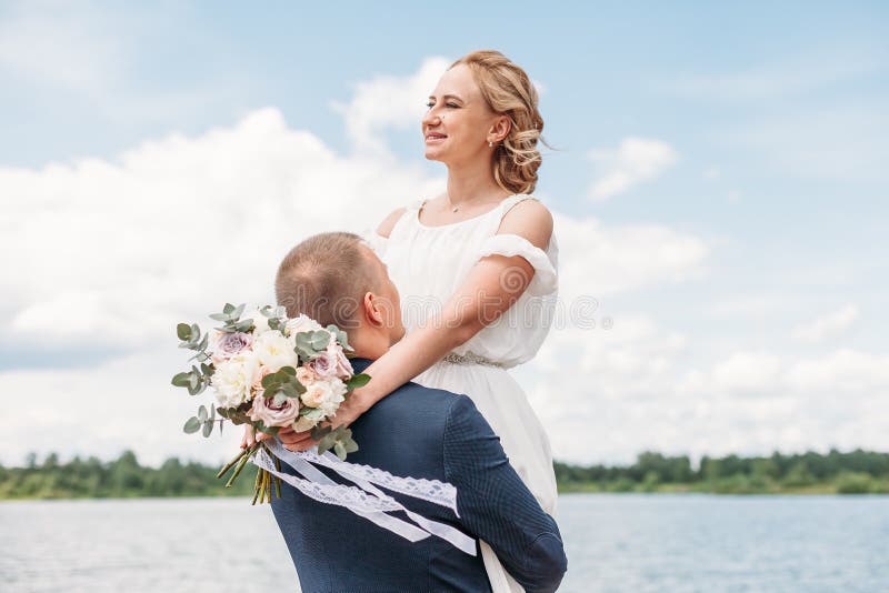 Groom lifted the bride in his arms against the blue sky and clouds. Groom lifted the bride in his arms against the blue sky and clouds.