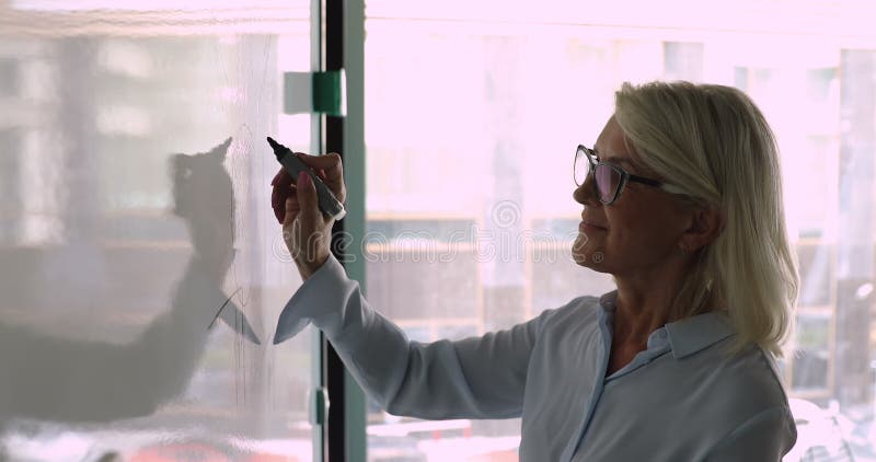 Le marqueur de la participation à la femme d'affaires âgé par juste milieu font des notes sur le tableau blanc banque de vidéos