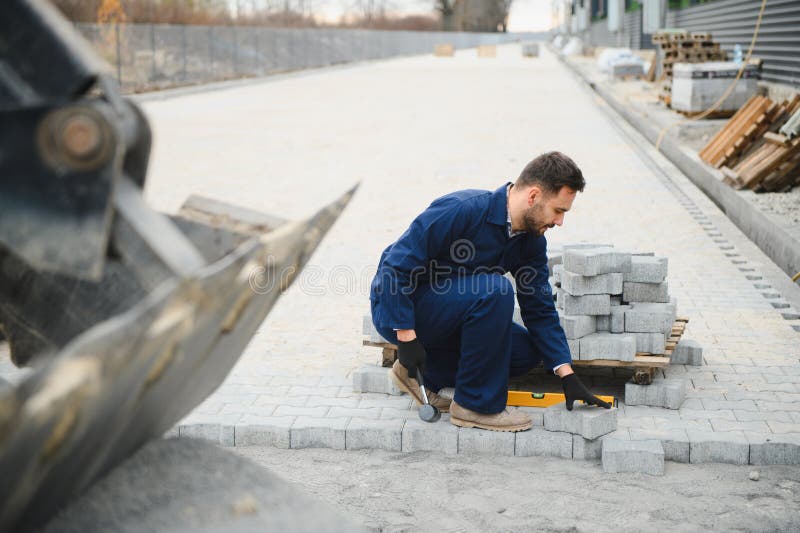 Le maître dans les gants pose des pavés en couches. Carrelage par un ouvrier professionnel du pavage. Lay gris photo libre de droits