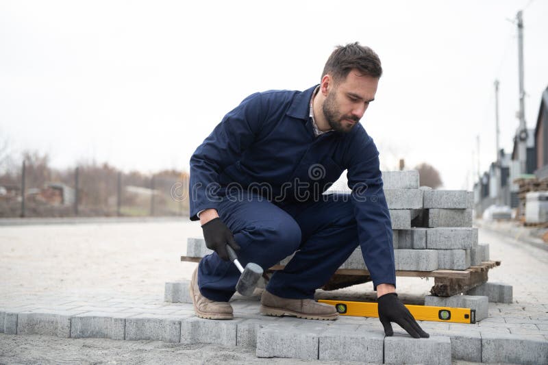 Le maître dans les gants pose des pavés en couches. Carrelage par un ouvrier professionnel du pavage. Lay gris photo libre de droits