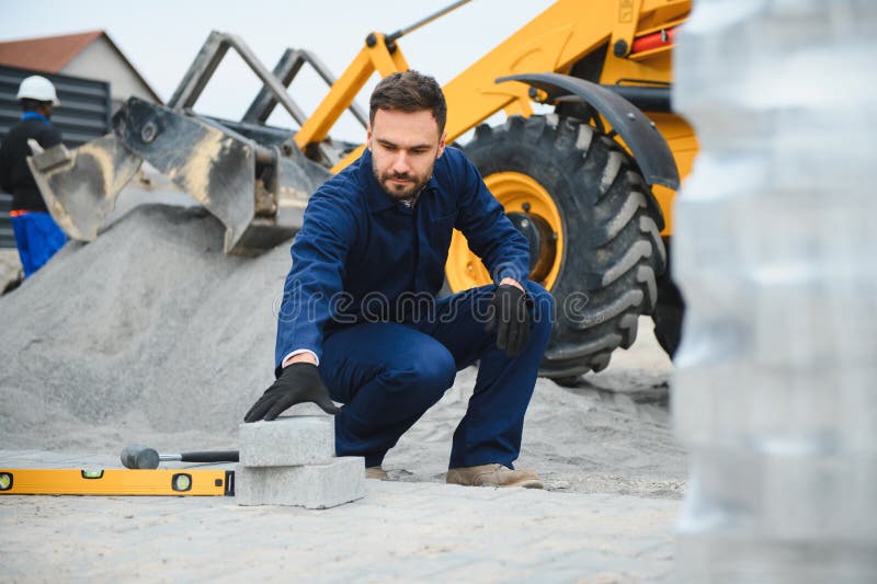 Le maître dans les gants pose des pavés en couches. Carrelage par un ouvrier professionnel du pavage. Lay gris photos stock