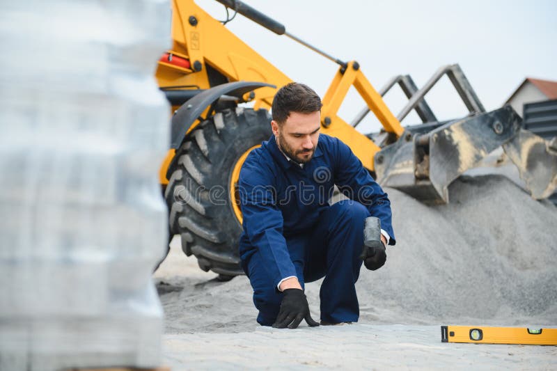 Le maître dans les gants pose des pavés en couches. Carrelage par un ouvrier professionnel du pavage. Lay gris photo stock