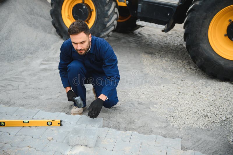 Le maître dans les gants pose des pavés en couches. Carrelage par un ouvrier professionnel du pavage. Lay gris photos stock