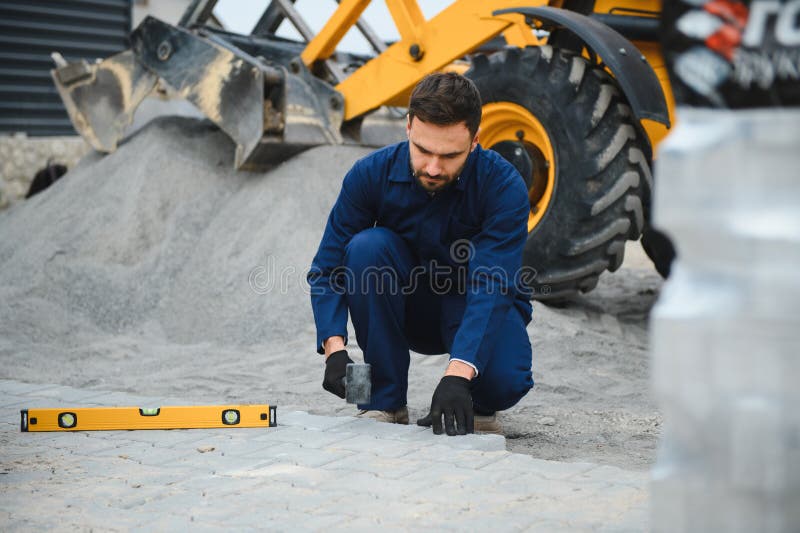 Le maître dans les gants pose des pavés en couches. Carrelage par un ouvrier professionnel du pavage. Lay gris image stock