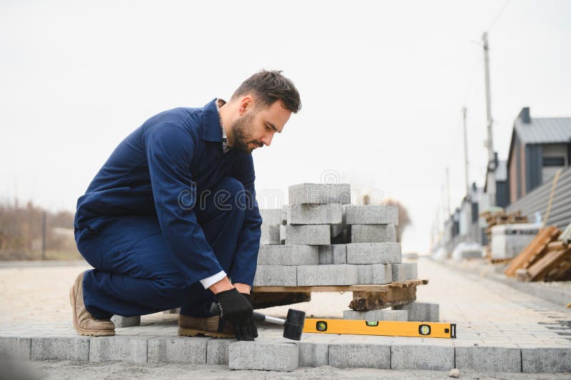 Le maître dans les gants pose des pavés en couches. Jetage de dalles de béton gris dans la cour de la maison sur le sable photo stock