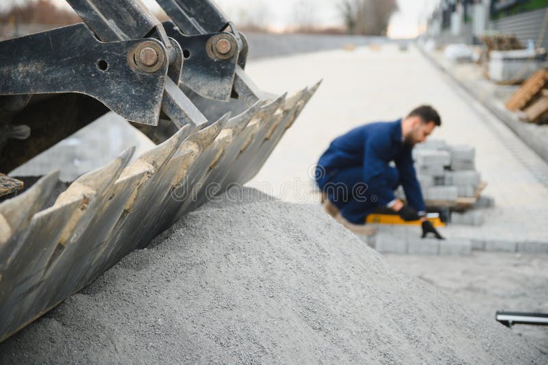 Le maître dans les gants pose des pavés en couches. Jetage de dalles de béton gris dans la cour de la maison sur le sable photos stock