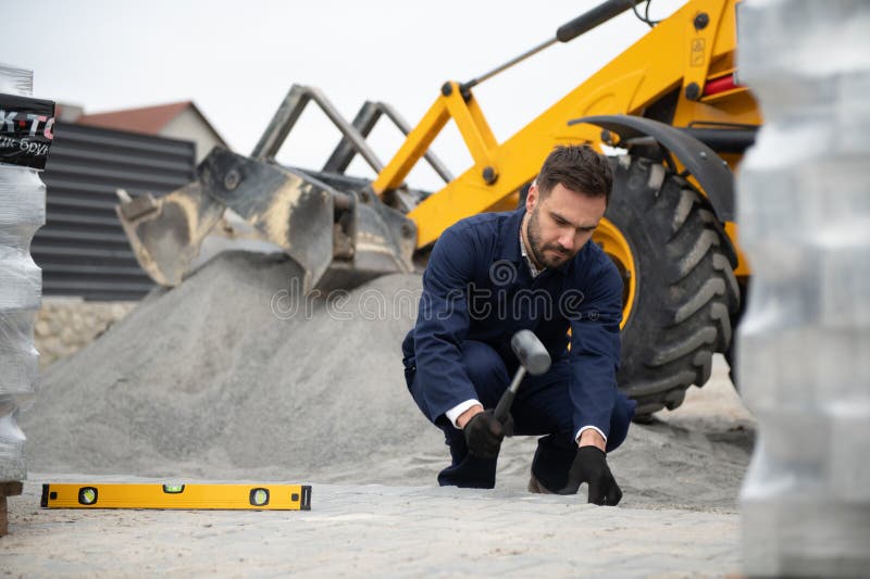Le maître dans les gants pose des pavés en couches. Jetage de dalles de béton gris dans la cour de la maison sur le sable photographie stock libre de droits