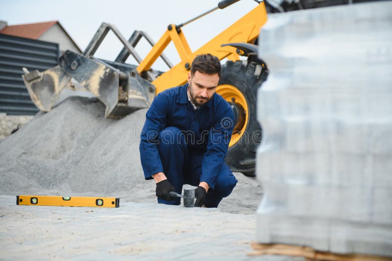 Le maître dans les gants pose des pavés en couches. Jetage de dalles de béton gris dans la cour de la maison sur le sable photo libre de droits