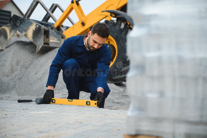Le maître dans les gants pose des pavés en couches. Jetage de dalles de béton gris dans la cour de la maison sur le sable photo stock