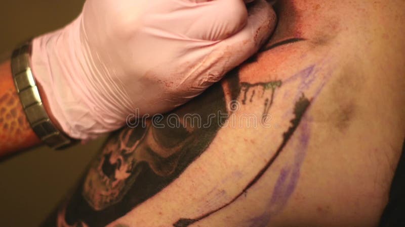 Le maître peint un tatouage avec un dessin de la mort sur l'épaule d'un homme