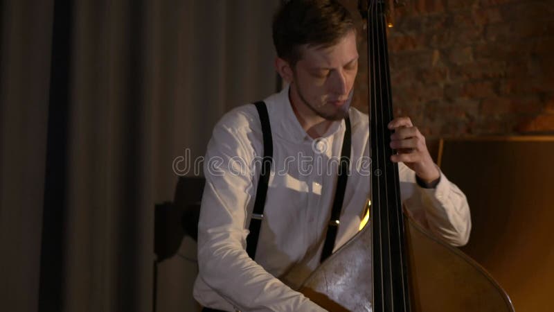 Le mec joue une double basse au studio. macro prise de vue des chaînes et timbre. le groupe musical joue au restaurant.