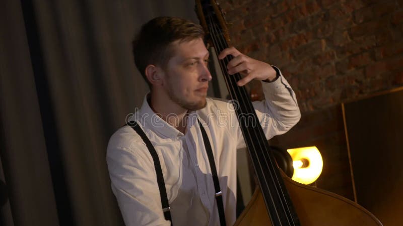 Le mec joue une double basse au studio. macro prise de vue des chaînes et timbre. le groupe musical joue au restaurant.