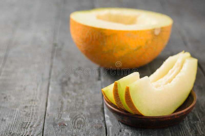 Le melon mûr rapièce sur une cuvette d'argile et la moitié d'un melon sur une table en bois photo stock Le melon mûr rapièce sur une cuvette d'argile et la moitié d'un melon sur une table en bois photo stock