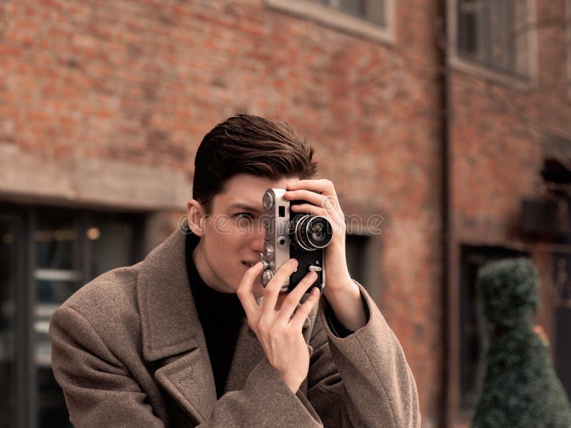 Le modèle de jeune homme dans un manteau photographie l'appareil-photo de vintage photographie stock Le modèle de jeune homme dans un manteau photographie l'appareil-photo de vintage photographie stock