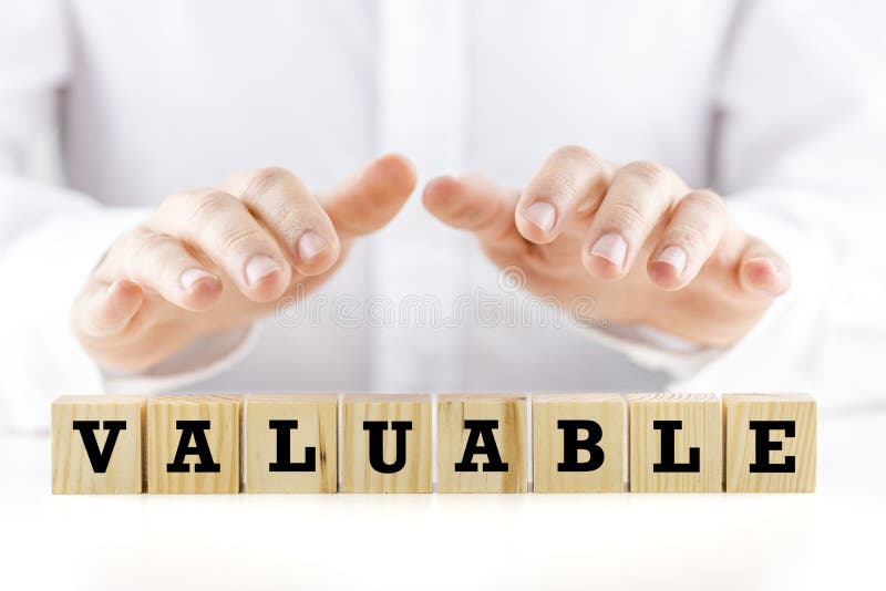 Conceptual image with the word - Valuable- on a row of natural wooden cubes or blocks with a man holding his hands cupped protectively over the top shielding them. Conceptual image with the word - Valuable- on a row of natural wooden cubes or blocks with a man holding his hands cupped protectively over the top shielding them