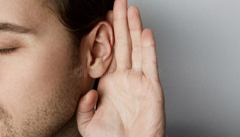 Le mâle de écoute tient sa main près de son oreille au-dessus de fond gris photos stock Le mâle de écoute tient sa main près de son oreille au-dessus de fond gris photos stock