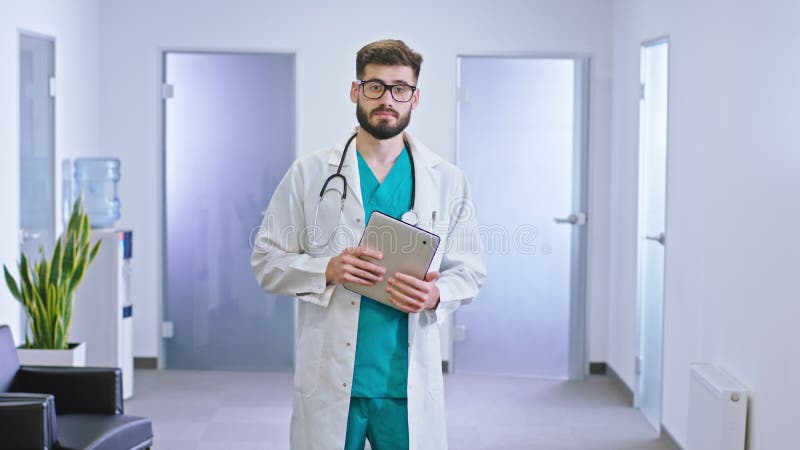 Le médecin charismatique d'homme devant la caméra dans le couloir d'hôpital jettent un coup d'oeil à son comprimé numérique regard