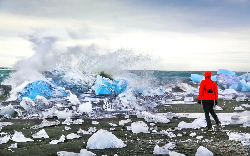 Le onde di sorveglianza della donna si schiantano contro gli iceberg alla laguna glaciale di Jokulsarlon vicino al parco nazionale