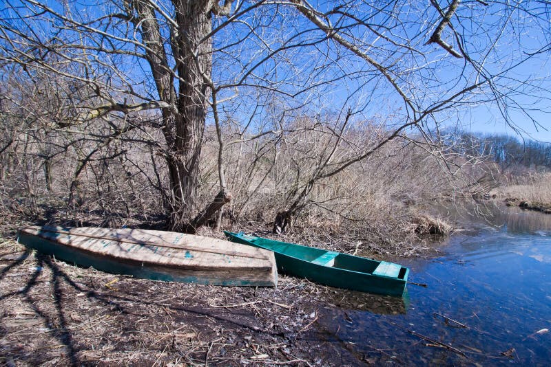 Le paysage tôt de ressort avec de petits vieux bateaux de pêche selfmade en bois donnent un coup de volée et les arbres nus su image libre de droits Le paysage tôt de ressort avec de petits vieux bateaux de pêche selfmade en bois donnent un coup de volée et les arbres nus su image libre de droits