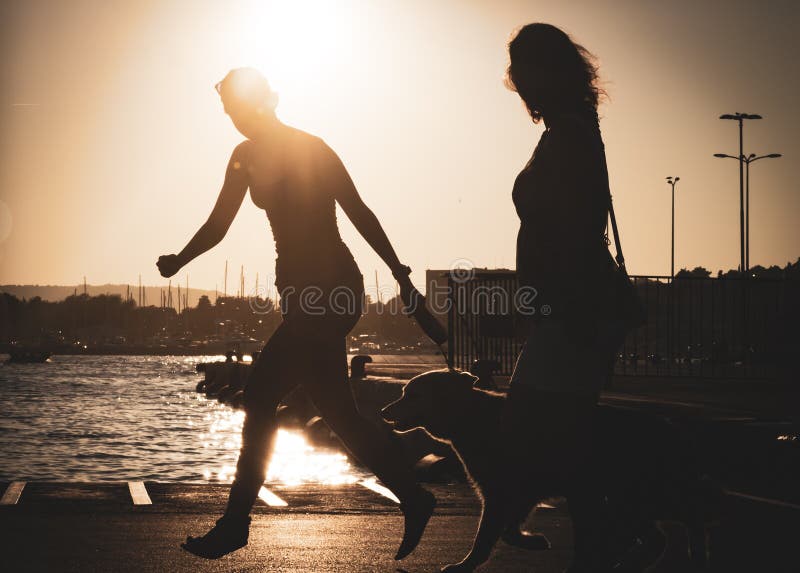 Le persor femelle et son chien, golden retriever fonctionne dans un port pendant le coucher du soleil images libres de droits Le persor femelle et son chien, golden retriever fonctionne dans un port pendant le coucher du soleil images libres de droits