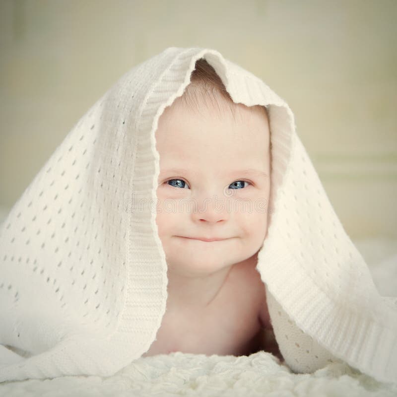 Le petit bébé avec la trisomie 21 s'est caché sous la couverture et les sourires sournoisement