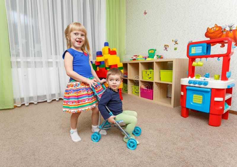 Le petit garçon et la fille jouent avec la poussette de jouet à la maison images libres de droits Le petit garçon et la fille jouent avec la poussette de jouet à la maison images libres de droits