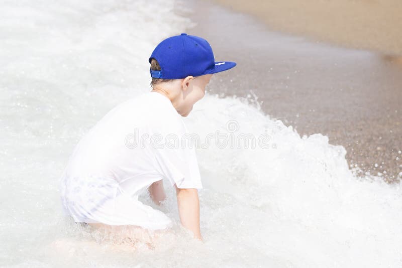 Le petit garçon joue avec de petites vagues sur la plage de mer Enfant des vacances tropicales d'été se baignant en eau de mer ch images stock Le petit garçon joue avec de petites vagues sur la plage de mer Enfant des vacances tropicales d'été se baignant en eau de mer ch images stock