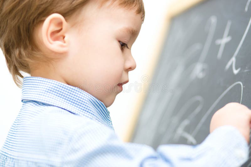 Le petit garçon écrit sur le tableau noir photos libres de droits Le petit garçon écrit sur le tableau noir photos libres de droits
