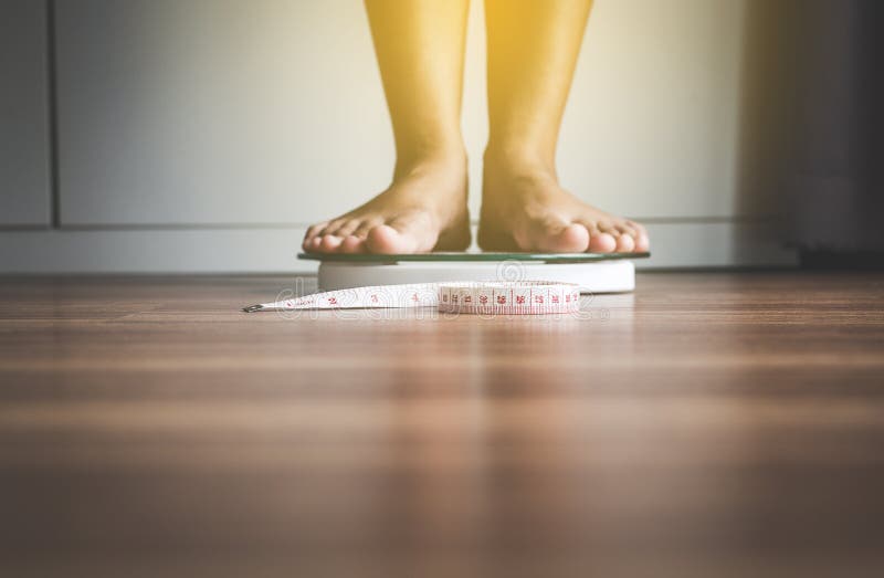 Le pied de femme se tenant dessus pèsent des échelles avec le ruban métrique dans le premier plan images stock Le pied de femme se tenant dessus pèsent des échelles avec le ruban métrique dans le premier plan images stock