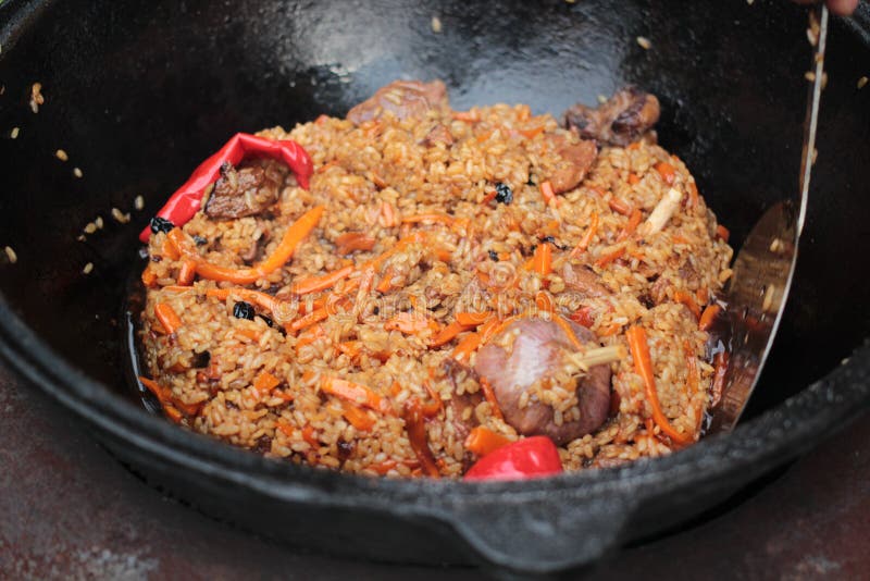 Le pilaf préparent en grande fonte noire avec des chefs remettent photographie stock Le pilaf préparent en grande fonte noire avec des chefs remettent photographie stock