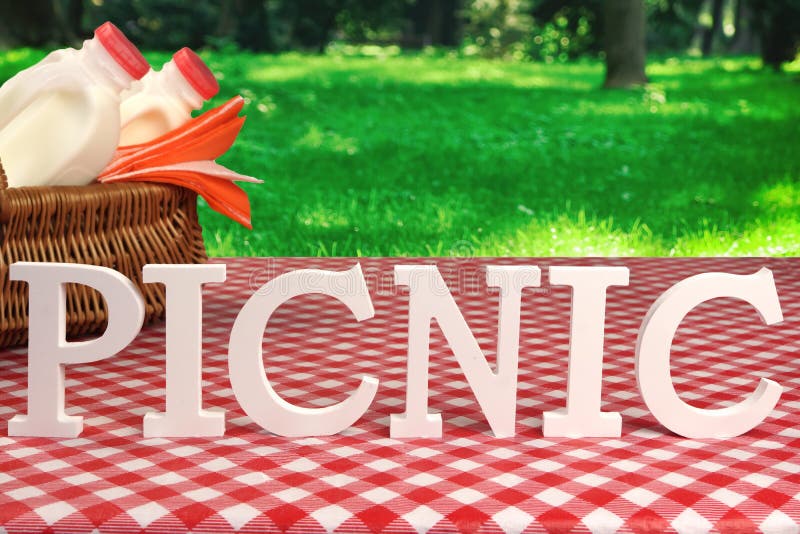 Sign Picnic Made From White Letters On The Table With Basket And Red Tablecloth In The Summer Garden. Sign Picnic Made From White Letters On The Table With Basket And Red Tablecloth In The Summer Garden