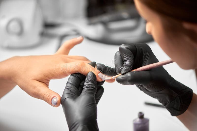 Le plan rapproché du manucure principal remet appliquer le vernis violet-clair sur des clous de femme de client utilisant la bros images stock Le plan rapproché du manucure principal remet appliquer le vernis violet-clair sur des clous de femme de client utilisant la bros images stock