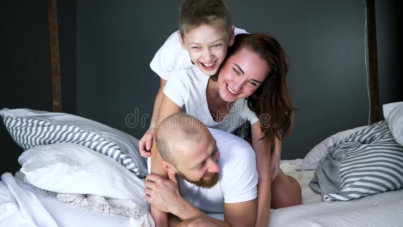 Le portrait de la famille heureuse dans le T-shirts se trouvent sur l'un l'autre sur le lit à la maison dans la chambre à coucher